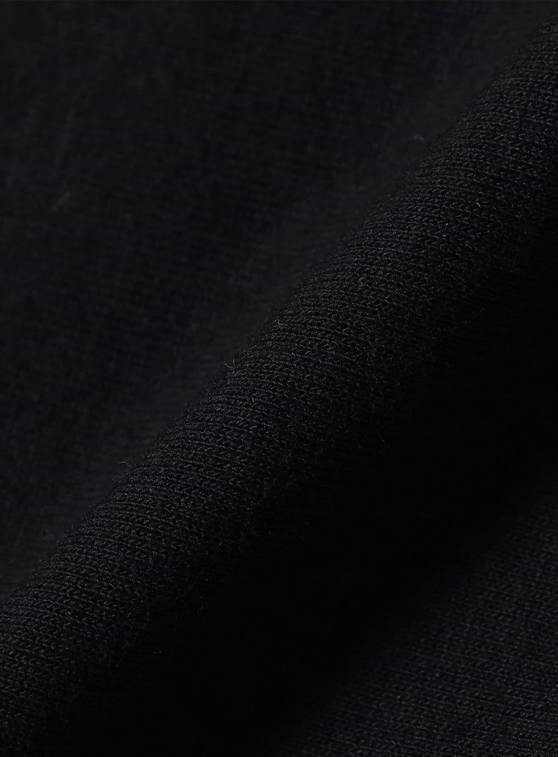 Close-up of [Exclusive] Champion Reverse Weave® Wide-Leg Shorts by CHAMPION, focusing on the black lightweight jersey fabric’s textured weave and a soft fold casting a diagonal shadow across the image.