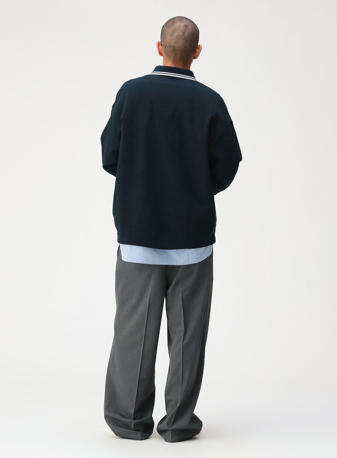 A person seen from behind, wearing a black [Exclusive] BEAMS x Fred Perry Pique Long Sleeve Polo Shirt with white collar tipping layered over a light blue shirt and gray trousers.