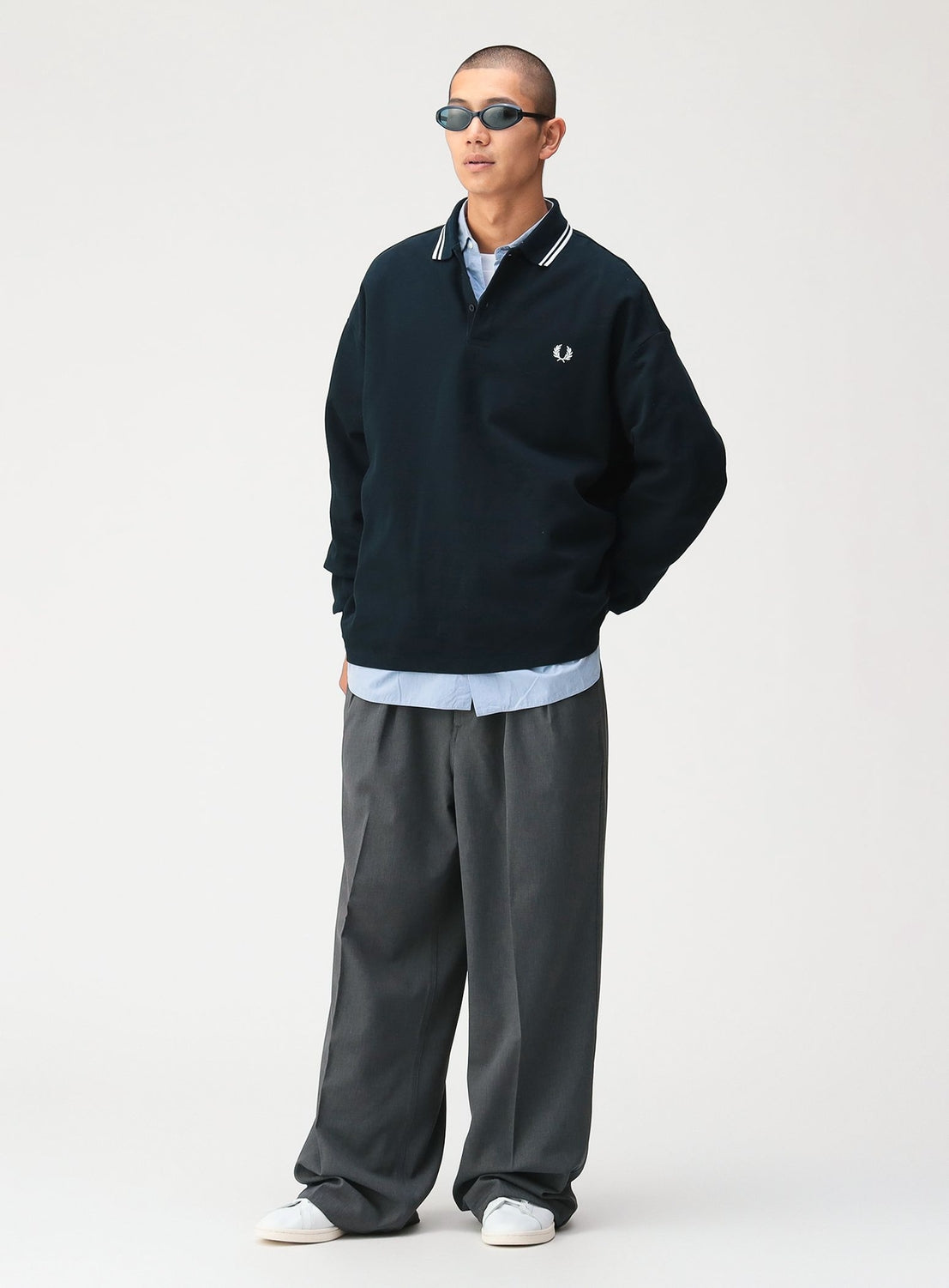 A person wearing an [Exclusive] BEAMS x Fred Perry Pique Long Sleeve Polo Shirt with a white-striped twin-tip collar over a light blue button-up shirt, paired with gray pleated trousers and white sneakers.