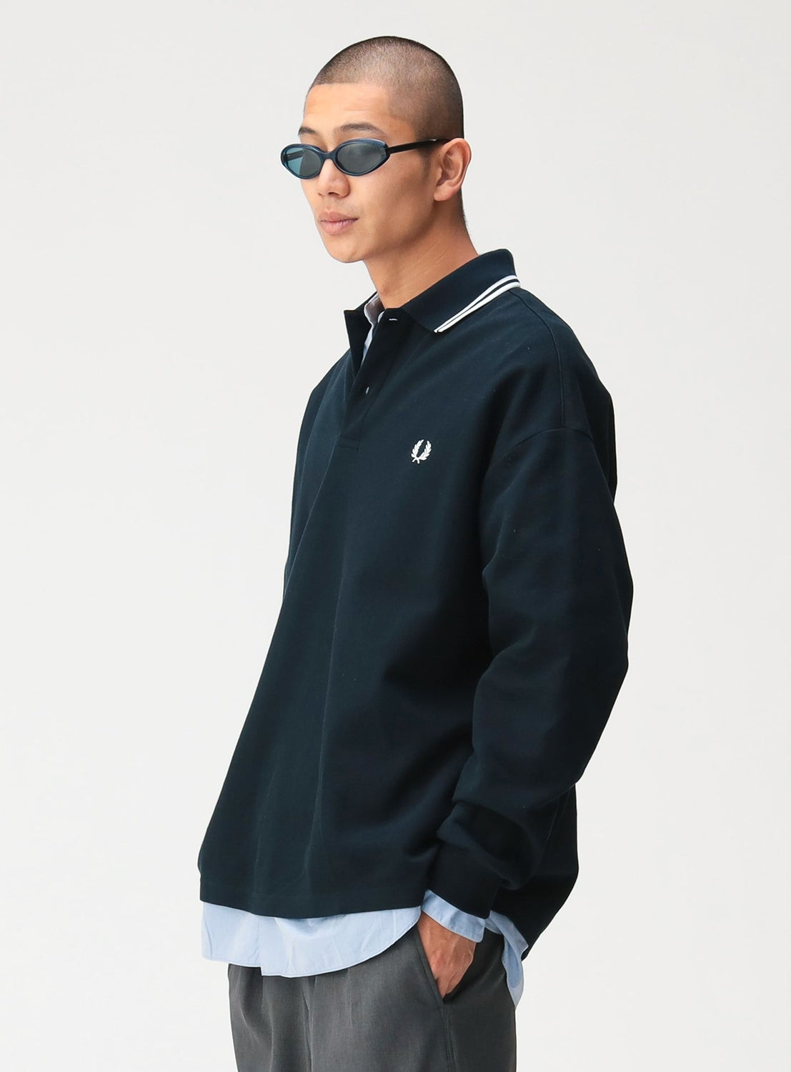A person wears an [Exclusive] BEAMS x Fred Perry Pique Long Sleeve Polo Shirt, a dark long-sleeve polo in a box silhouette featuring a white twin-tip collar and a laurel wreath logo on the chest.
