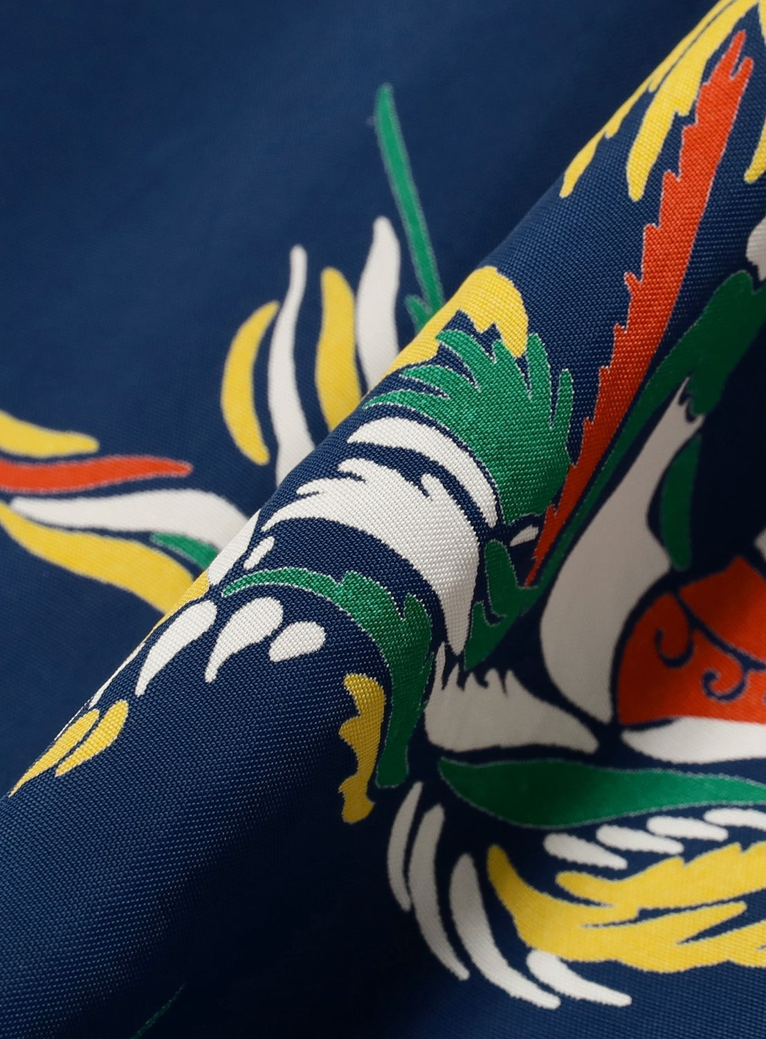 Close-up of blue fabric from the SUN SURF Sleeveless Cami Dress, featuring a vibrant Hawaiian dragon print in green, white, yellow, and orange—ideal standout resort wear from SUN SURF.
