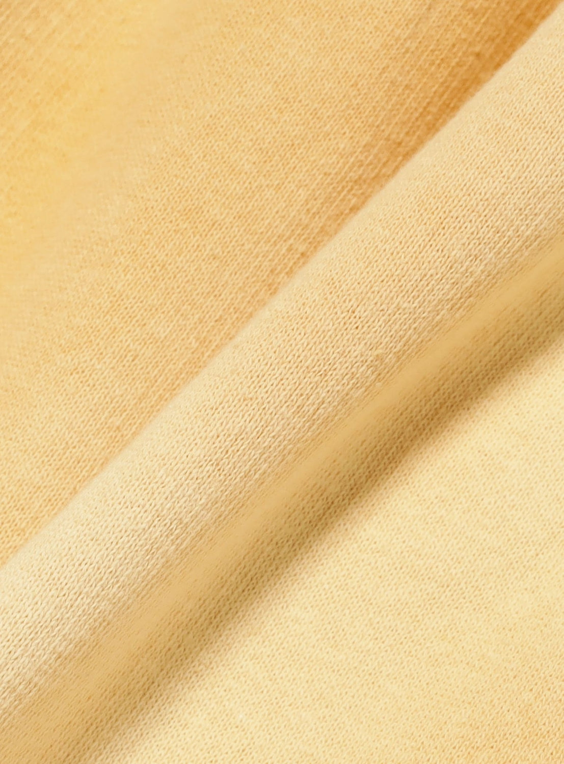 A close-up of the soft, light yellow loopback cotton fabric from INSCRIRE’s Yellow Faded Sweat Wide Pants showcases its visible weave texture and gentle folds, highlighting the smooth and cozy material—ideal for creating vintage-inspired wide-leg sweatpants.