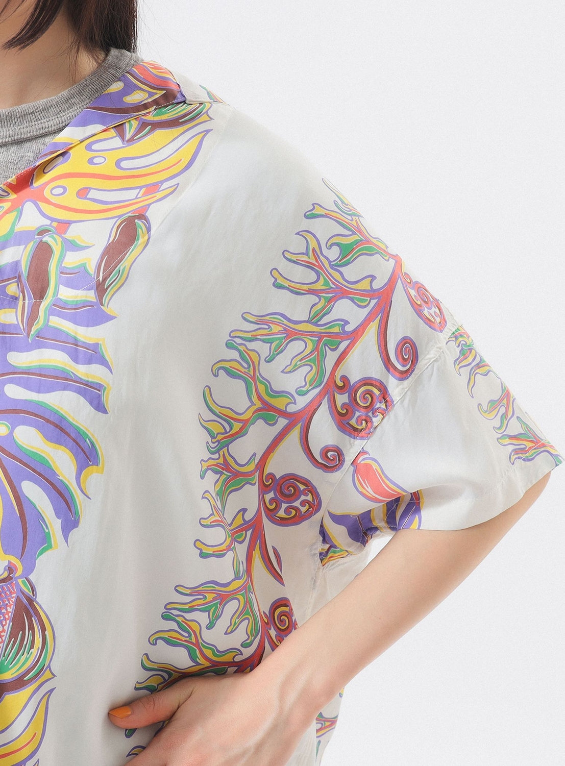A person wears the [Exclusive] SUN SURF x BEAMS BOY Sailor Shirt—an abstract, colorful piece inspired by Hawaiian prints from SUN SURF—shown from shoulders to waist with one hand on their hip.