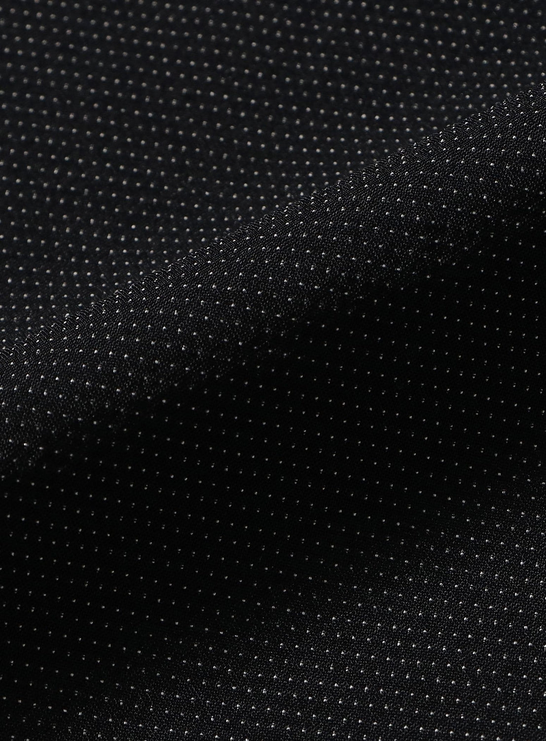 Close-up of the TEATORA Long Sleeve Cartridge Shirt in black, featuring wrinkle-resistant fabric with a fine, regular pattern of small white dots that forms a textured, grid-like appearance. Gentle folds in the material add depth and shadow—making this shirt an ideal travel companion to keep you looking polished on the go.