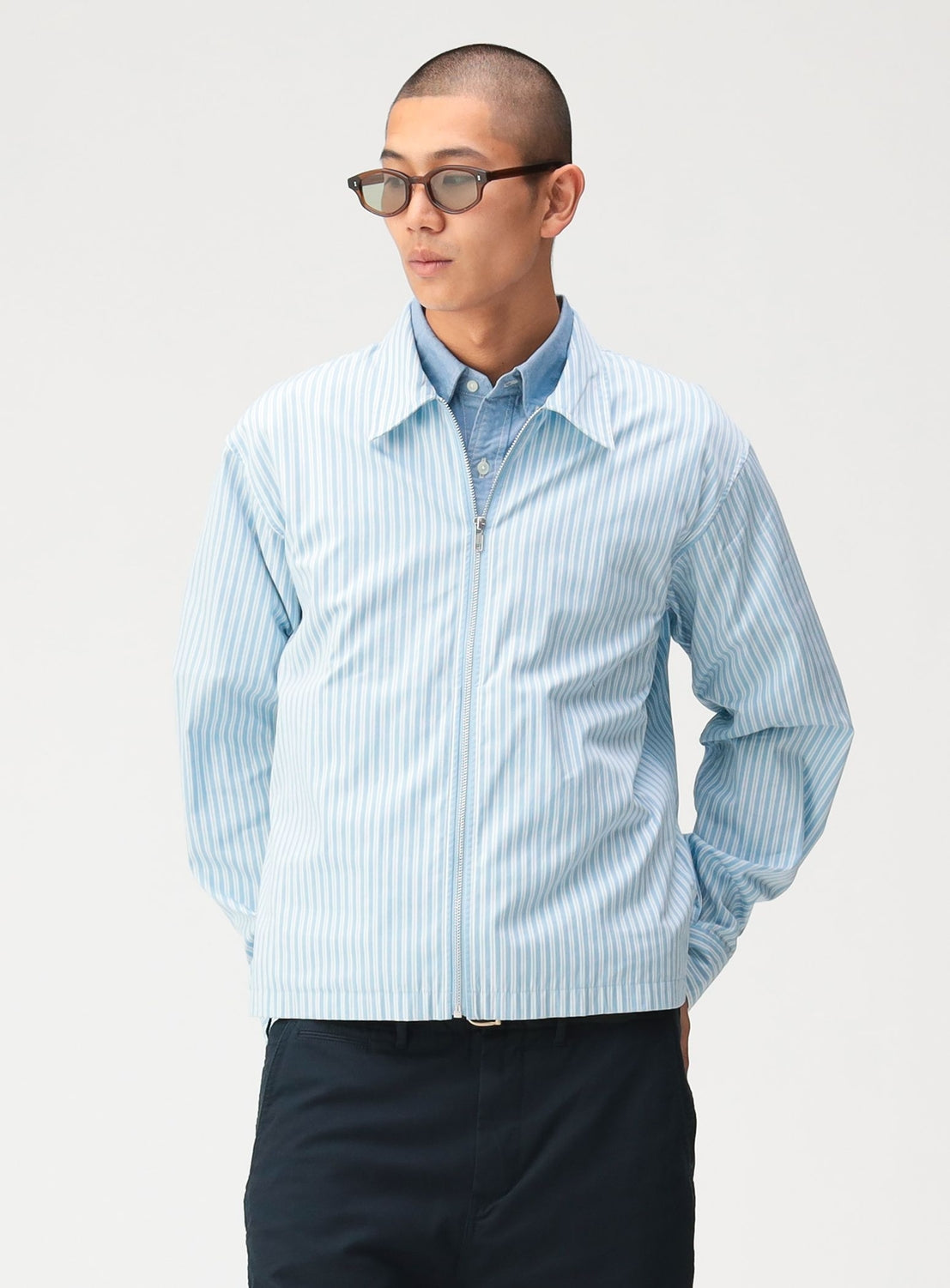 A man wearing a BEAMS Striped Zip-Up Shirt in light blue and white stripes over a button-down shirt.