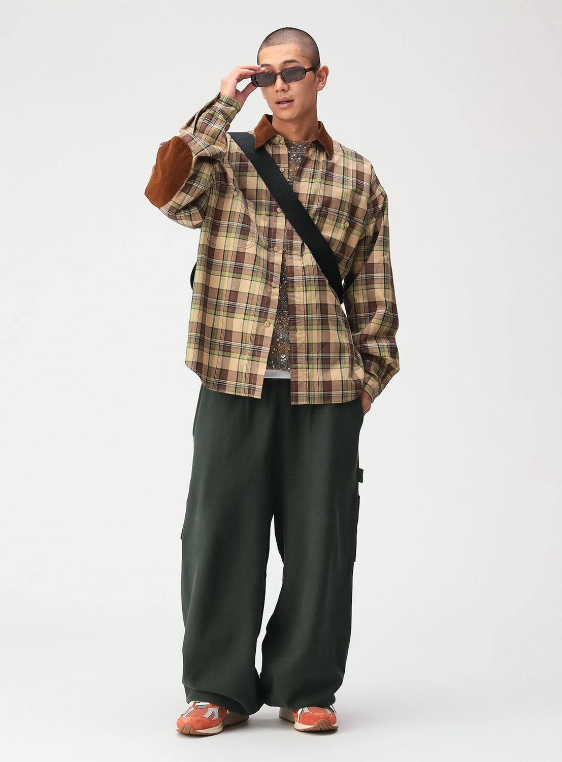 A man wearing a BEAMS Classic Check Work Shirt with a corduroy collar and brown elbow patches, styled with dark green loose-fit pants and orange sneakers.