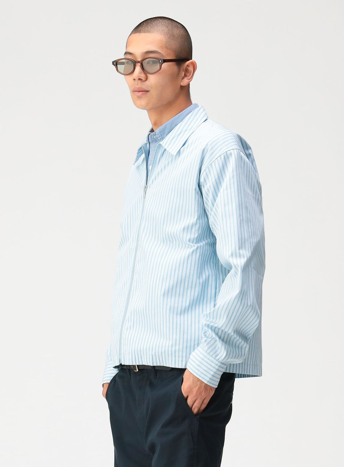 A man wearing a light blue and white striped BEAMS Striped Zip-Up Shirt over a collared shirt.