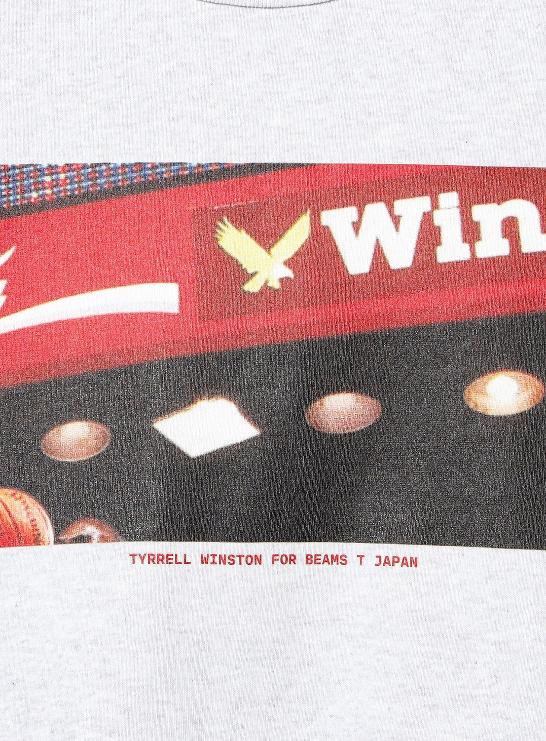 A close-up of the Tyrrell Winston - Win T-Shirt by BEAMS T features a partial Win sign with a yellow eagle logo and spotlights, along with text reading “TYRRELL WINSTON FOR BEAMS T JAPAN” at the hem, highlighting the dynamic WIN SPORT design in this exclusive BEAMS collaboration.