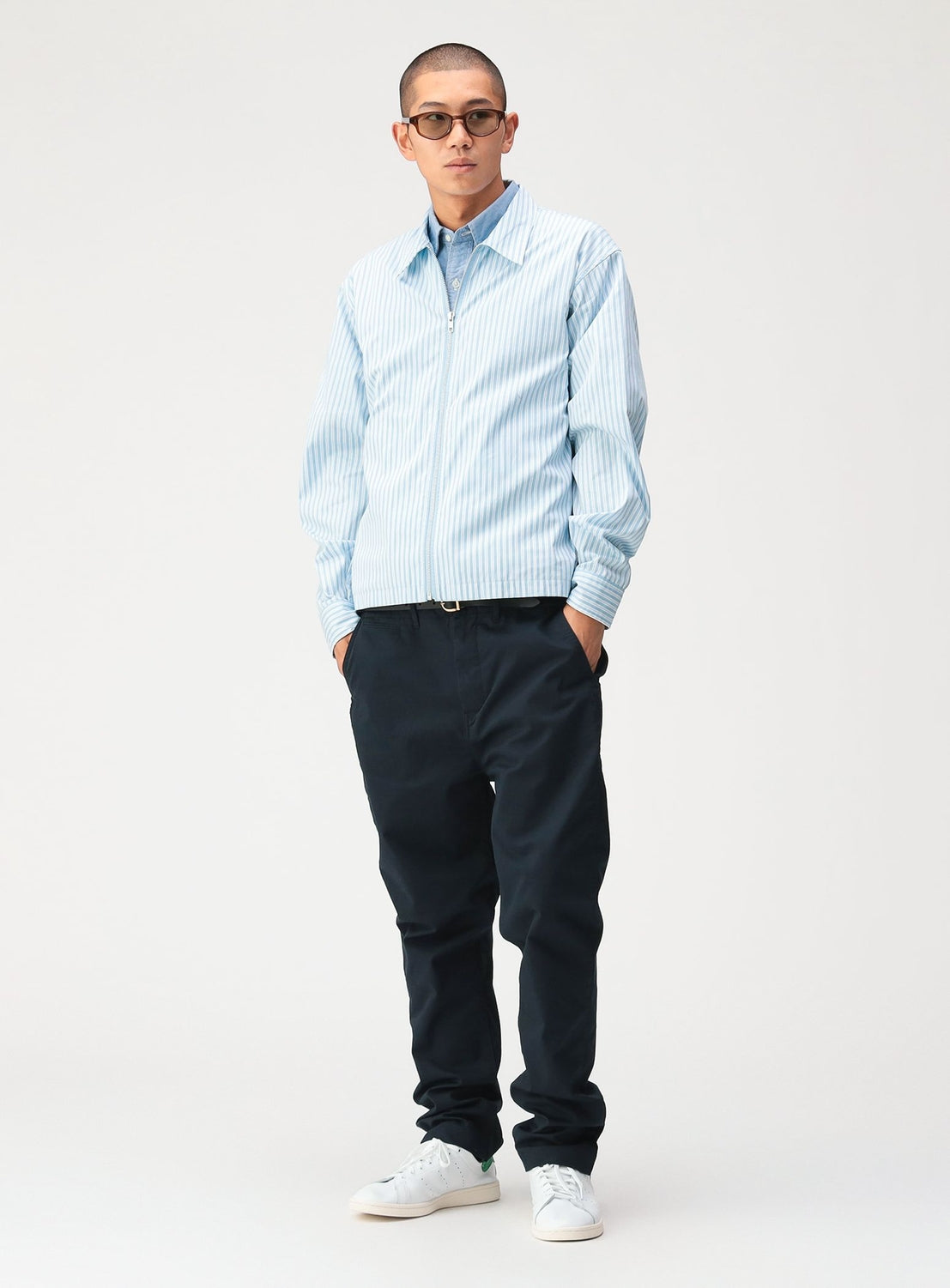 A man wearing a BEAMS Striped Zip-Up Shirt in light blue and white stripes over a blue collared shirt, paired with dark trousers and white sneakers.