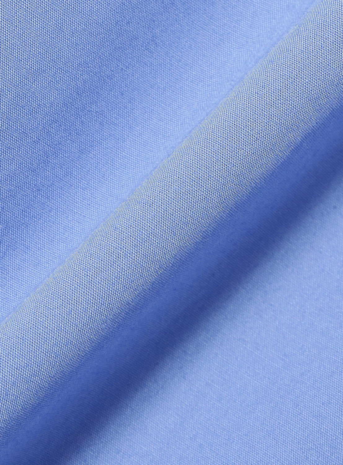 Close-up of light blue woven fabric with a visible diagonal fold, showing fine texture and soft shading—ideal for crafting the TTT MSW Regular Collar Shirt, designed for a genderless look with a relaxed silhouette and modern fit.