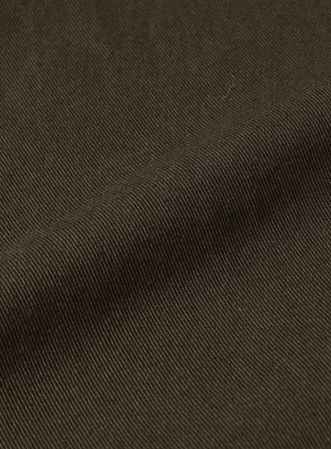 Close-up of dark brown, diagonally-ribbed fabric reveals a fine texture and subtle folds. The material looks smooth and tightly woven, characteristic of the BEAMS Basic Twill Easy Pants—relaxed-fit cotton twill, perfect for everyday comfort and style.