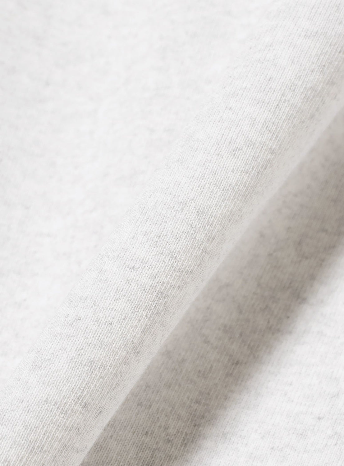 A close-up of the TTT MSW Logo T-Shirt by TTT MSW, highlighting its light gray, 100% cotton fabric with a soft, fine texture and subtle diagonal folds that reveal the delicate weave details.