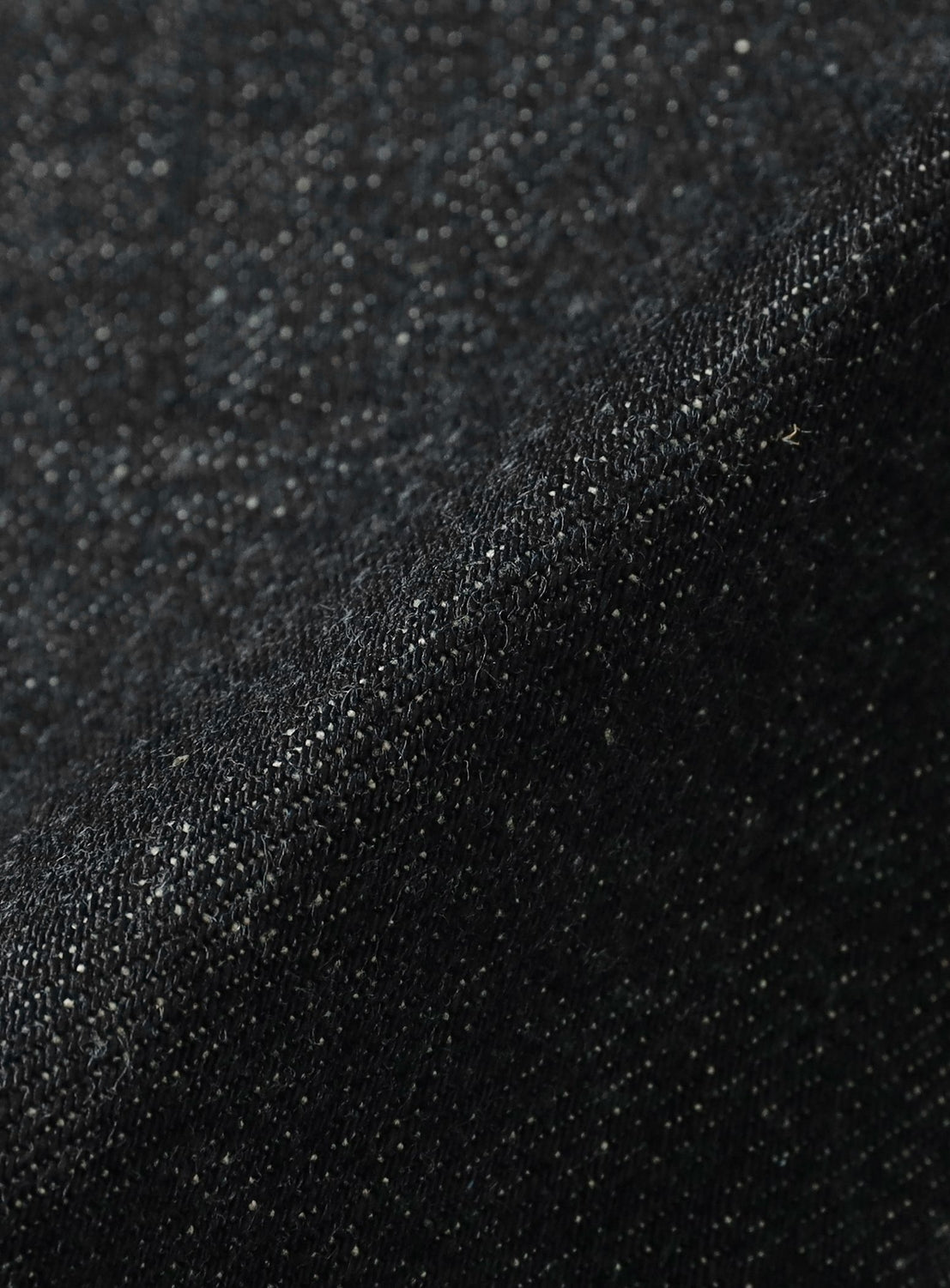 Close-up of dark, textured fabric with visible weave and subtle specks, capturing the tactile appeal of selvedge denim in SUGARHILL’s Classic Denim Pants.