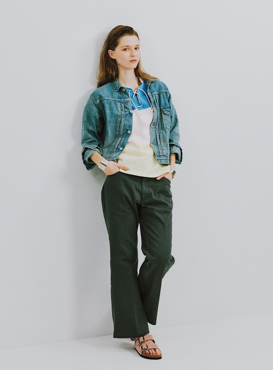 Woman wearing a denim jacket and green pants against a plain background