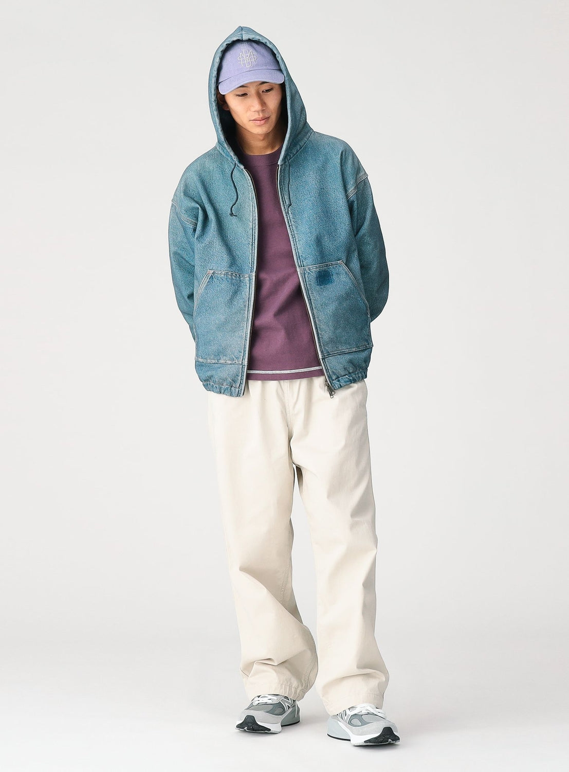 A person stands in a relaxed pose against a plain background, wearing a blue hooded denim jacket, a purple shirt, BEAMS Basic Twill Easy Pants with an adjustable waistband for a relaxed fit, gray sneakers, and a light purple cap.