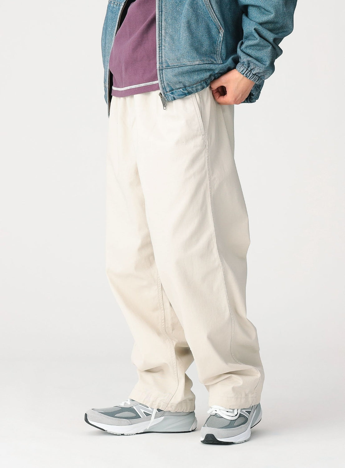 A person stands against a plain white background wearing a blue denim jacket, a purple shirt, gray sneakers, and BEAMS Basic Twill Easy Pants in cream with an adjustable waistband.