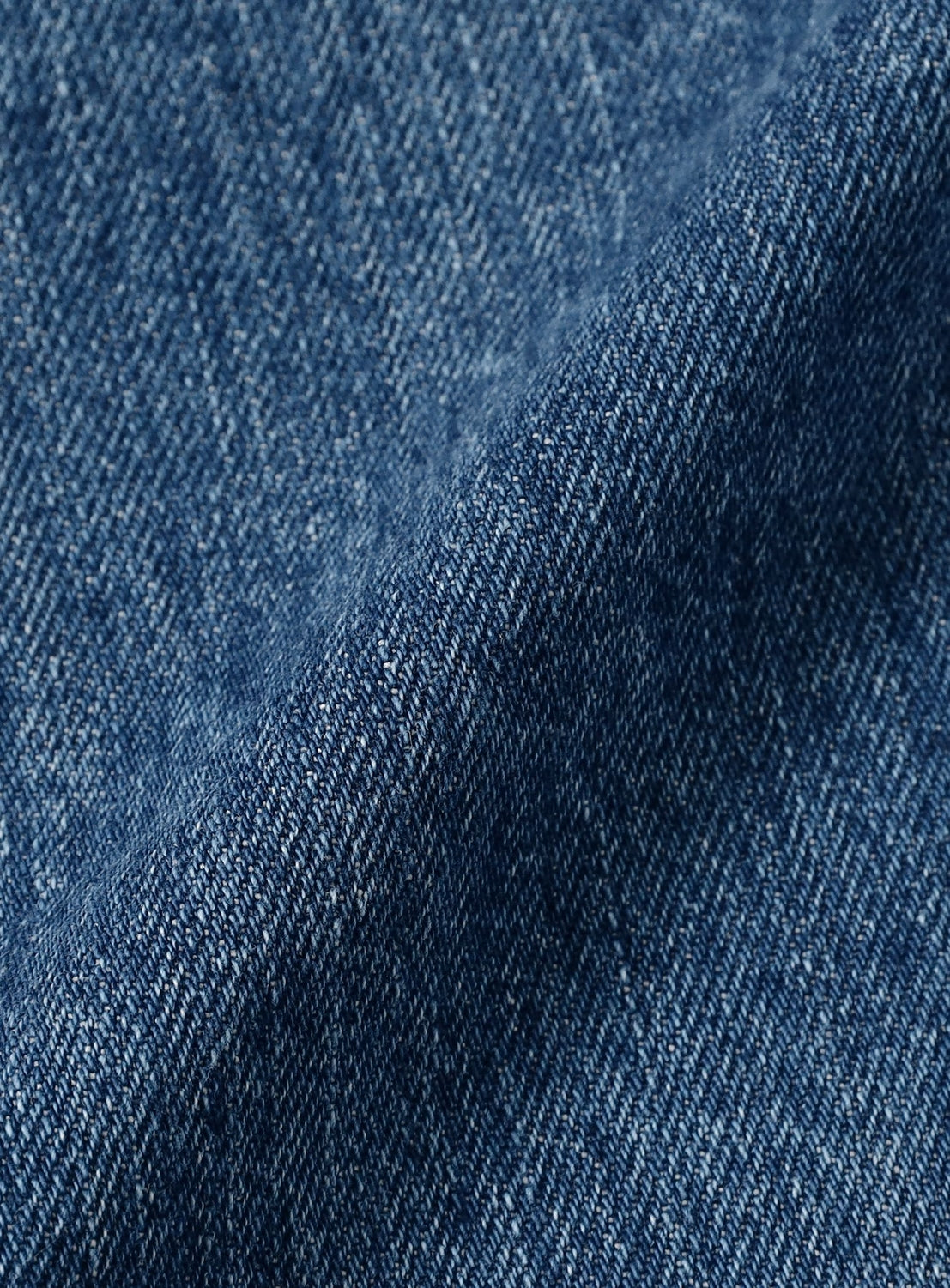 Close-up of blue Bandana Embroidery Denim Pants by NOMARHYTHM TEXTILE, showcasing the visible weave texture and a folded crease running diagonally across the fabric, which highlights the premium quality characteristic of Japanese-made jeans.