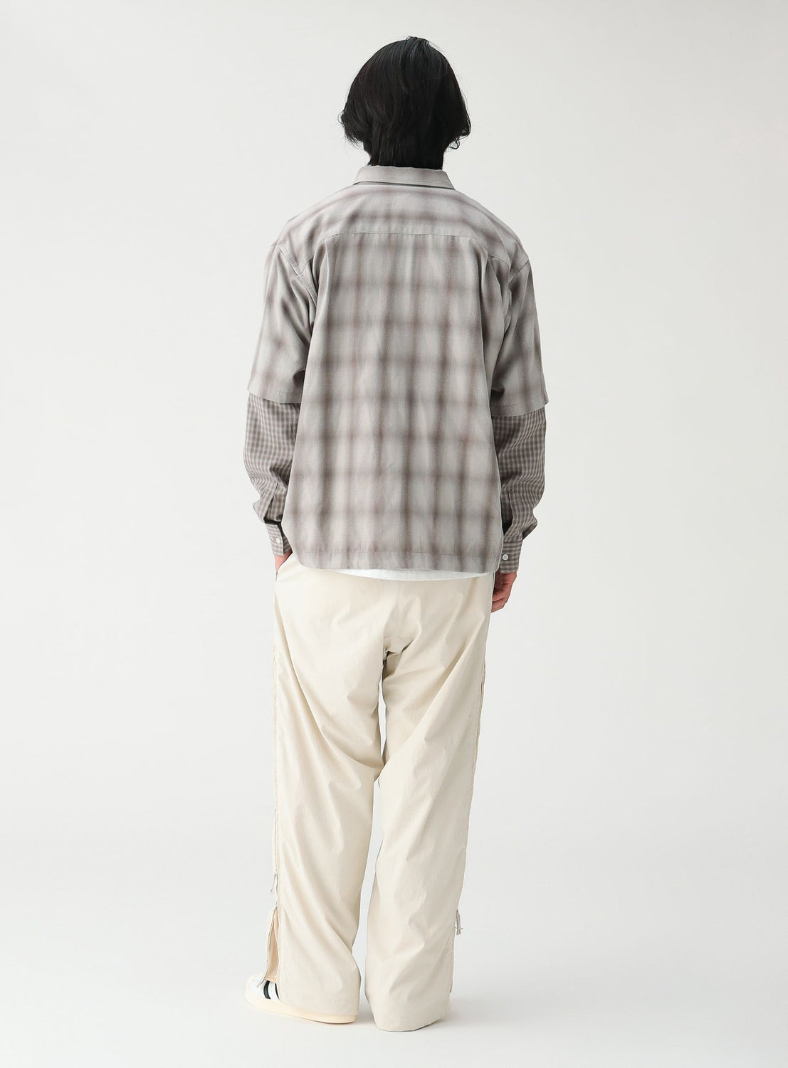 A person seen from behind wearing a wide-fit, grey plaid BEAMS Layered Check Shirt paired with light-colored trousers.