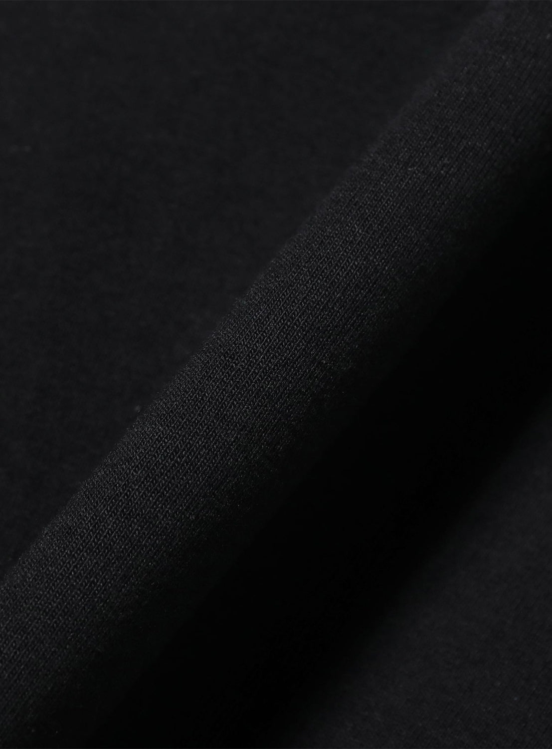 Close-up of the TTT MSW Logo T-Shirt in black, partially folded to reveal its smooth, soft texture. The lighting accentuates the shirt’s fine weave, while an embroidered Triple T logo from TTT MSW subtly enhances its refined appearance.