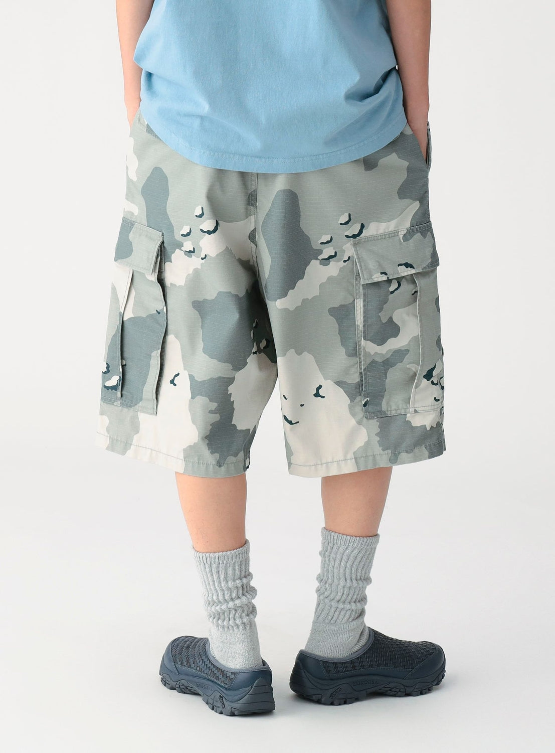 Person wearing camouflage shorts and blue shoes on a white background