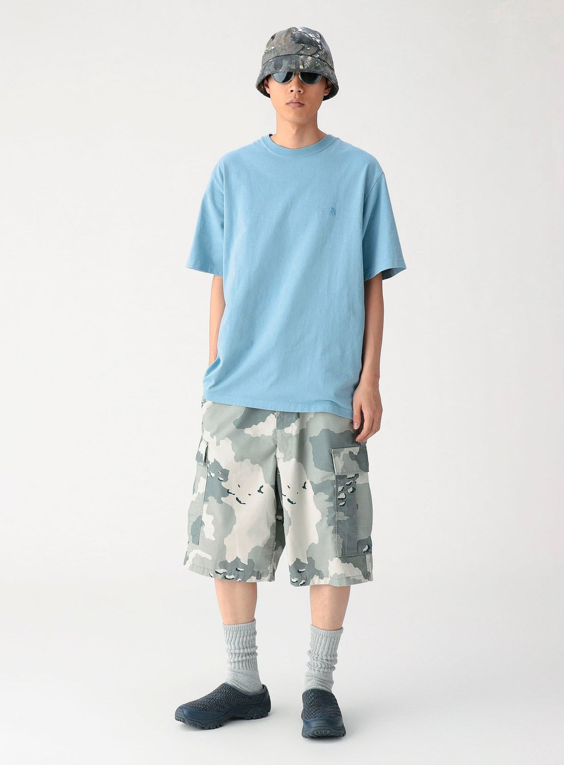 Person wearing a light blue t-shirt, camouflage shorts, and a cap on a white background