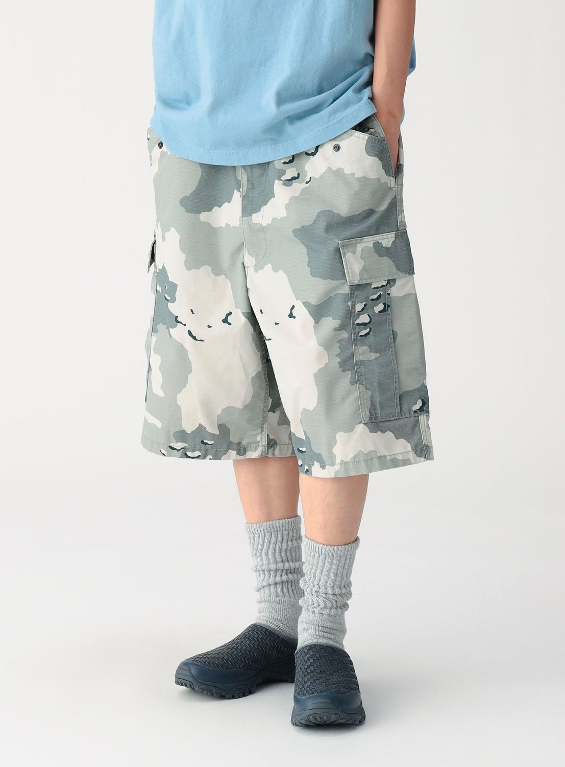 Person wearing camouflage shorts and gray socks on a white background