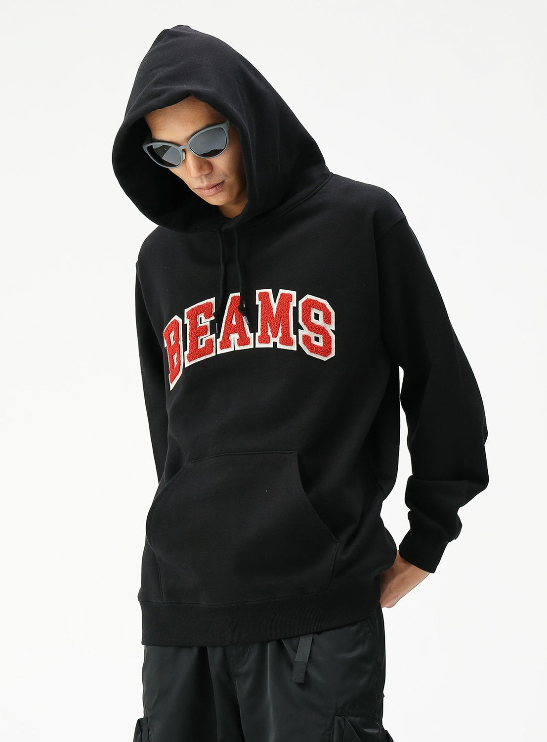 A person wearing a black BEAMS Basic Hoodie, black sunglasses, and black pants stands against a plain white background.
