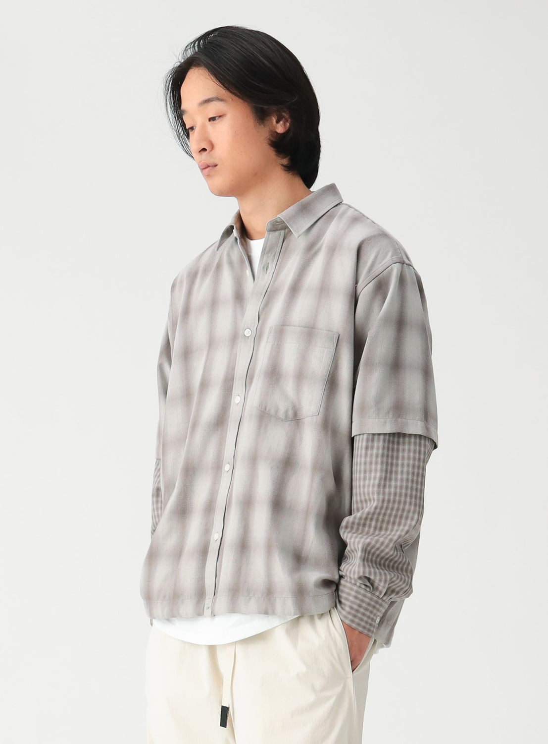 A person wears a BEAMS Layered Check Shirt, a wide-fit, faux-layered top featuring a gray, blurred-plaid short-sleeve button-down over long, fine-check sleeves.