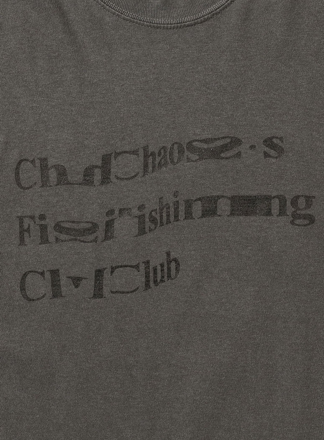 A dark, pigment-dyed OCG T-Shirt by Chaos Fishing Club featuring distorted, partially obscured black text that appears to read “Chaoss Fishing Club.” Some letters are warped and unclear, giving it an authentic vintage streetwear vibe.