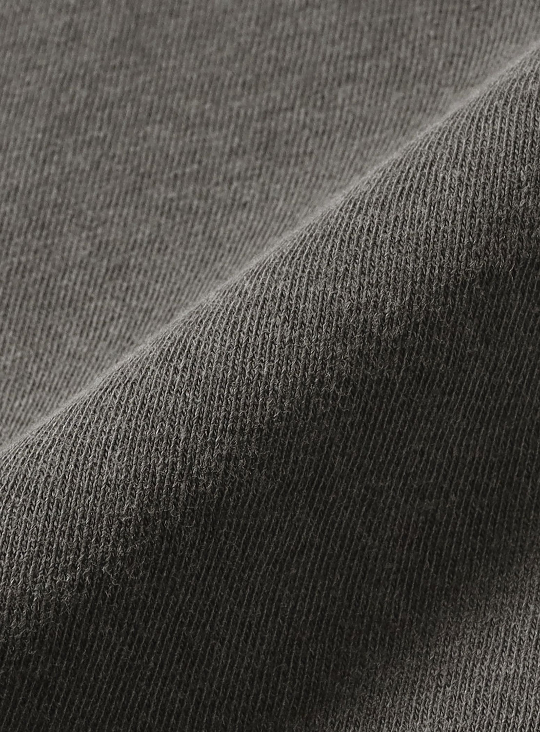 Close-up of gray, ribbed fabric from the OCG T-Shirt by Chaos Fishing Club, featuring a diagonal fold that highlights the detailed knit texture and weave pattern—evoking vintage streetwear vibes and capturing the subtle, worn-in appearance often seen with pigment-dyed techniques.