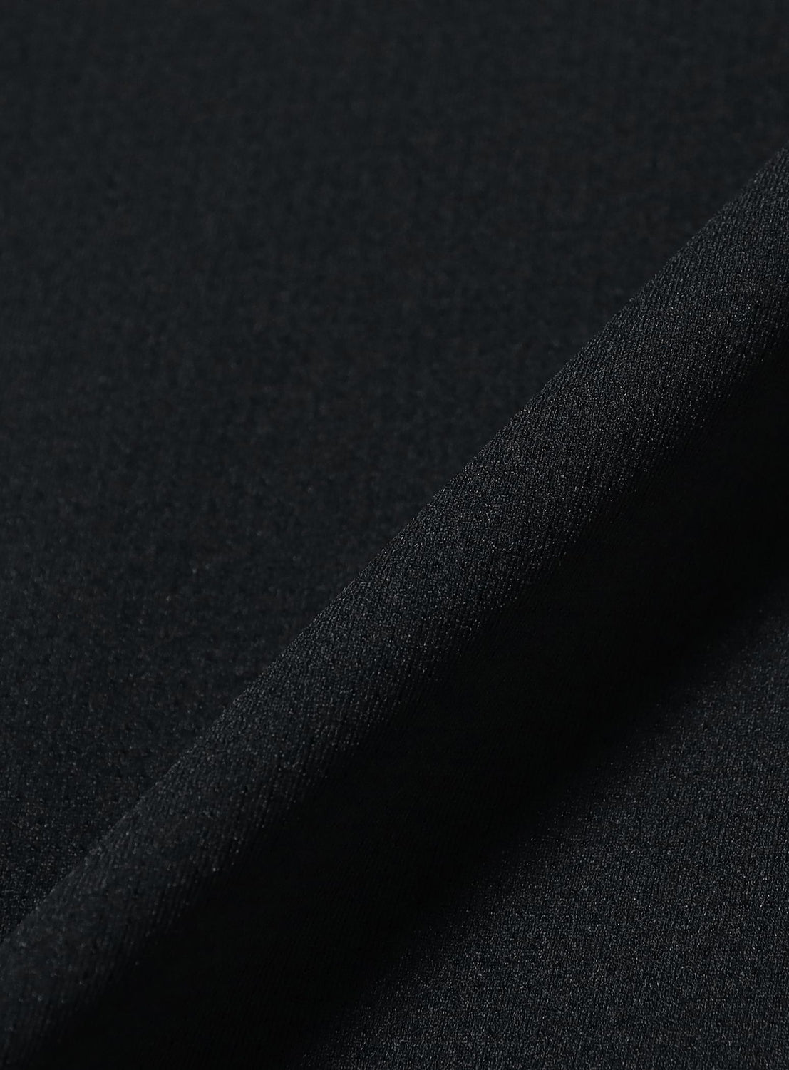 Close-up of the black fabric used in the BEAMS Relaxed Fit Dynamic Dry Crew Neck T-Shirt, featuring a subtle texture and a folded edge running diagonally across the image; this lightweight material offers excellent moisture-wicking properties.