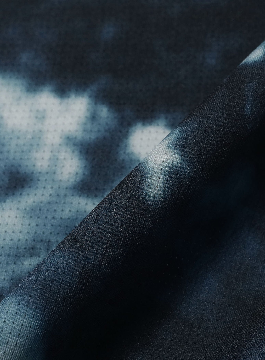 Close-up of a dark blue and white tie-dye fabric with a subtle dotted texture, softly folded diagonally across the image. The BEAMS Relaxed Fit Dynamic Dry Crew Neck T-Shirt is crafted from lightweight, moisture-wicking material to keep you cool and comfortable all day.
