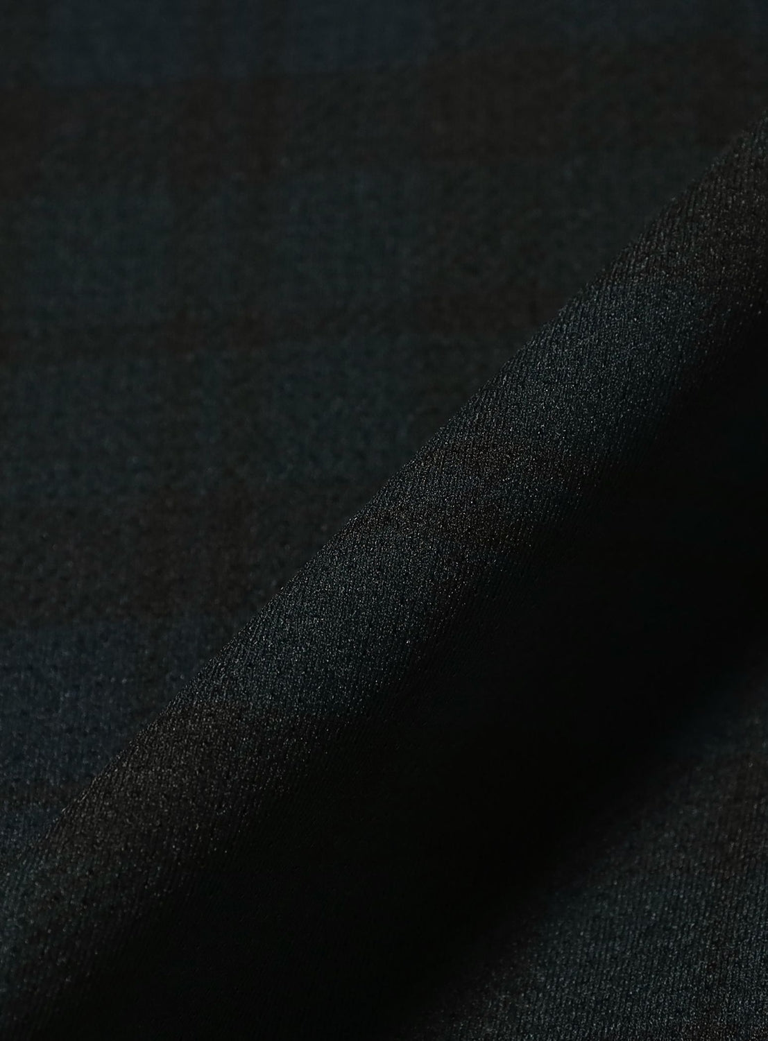 A close-up of the BEAMS Relaxed Fit Dynamic Dry Crew Neck T-Shirt reveals its dark plaid fabric, featuring a subtle checkered pattern with soft folds and a textured weave—perfect for a lightweight tee that combines style and comfort. The fabric’s construction offers excellent moisture-wicking properties, ensuring you stay fresh all day long.