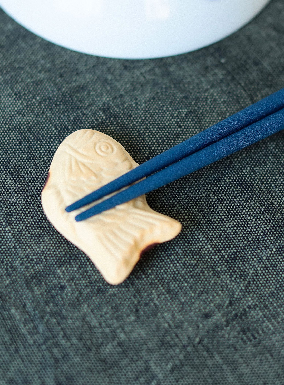 Fish-shaped chopstick rest with blue chopsticks on a textured surface