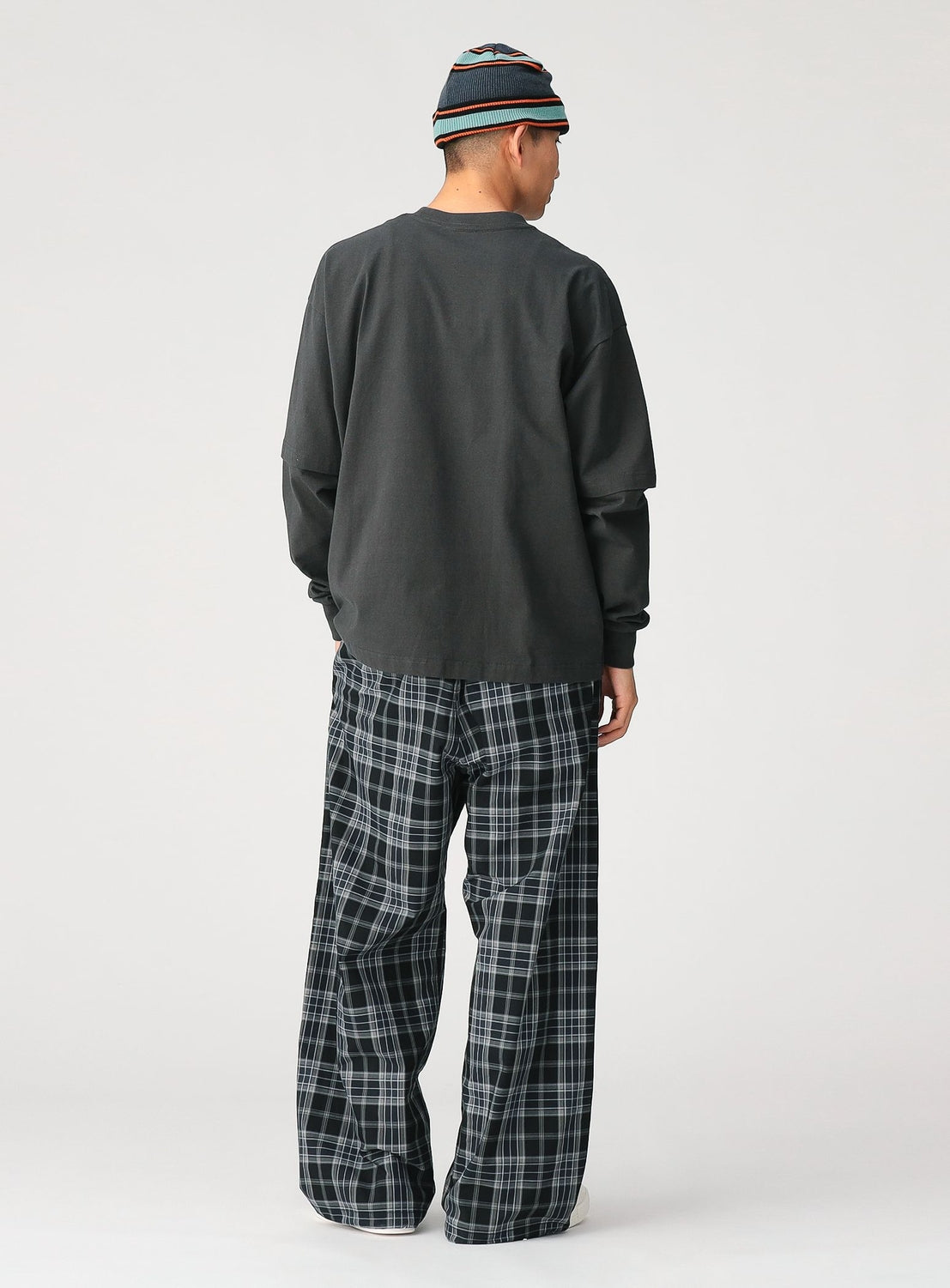 A person faces away, modeling the CHAMPION [Exclusive] Mock Layered Long-Sleeve T-Shirt, paired with loose plaid pants and a striped beanie, set against a plain background for a relaxed, comfortable fit.