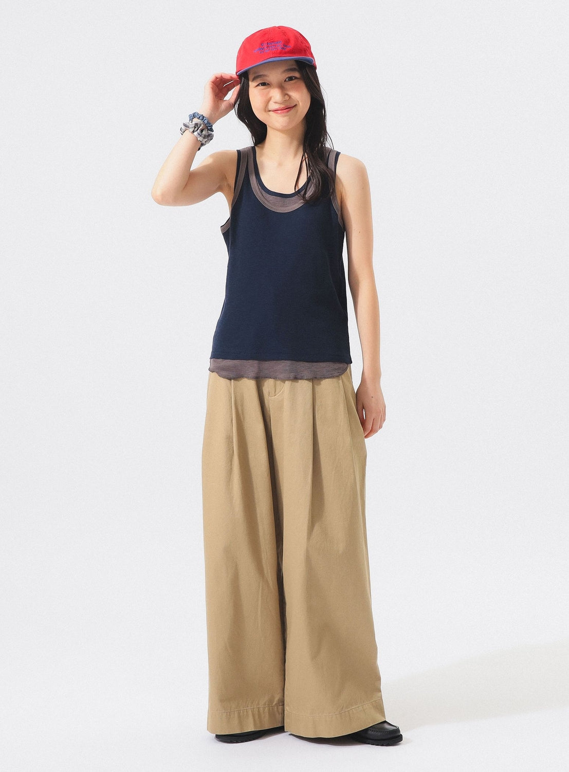 Wearing the BEAMS BOY Layered Rib Tank Top, a woman in a red cap and wide beige pants stands smiling with one hand touching her hat against a plain white background.