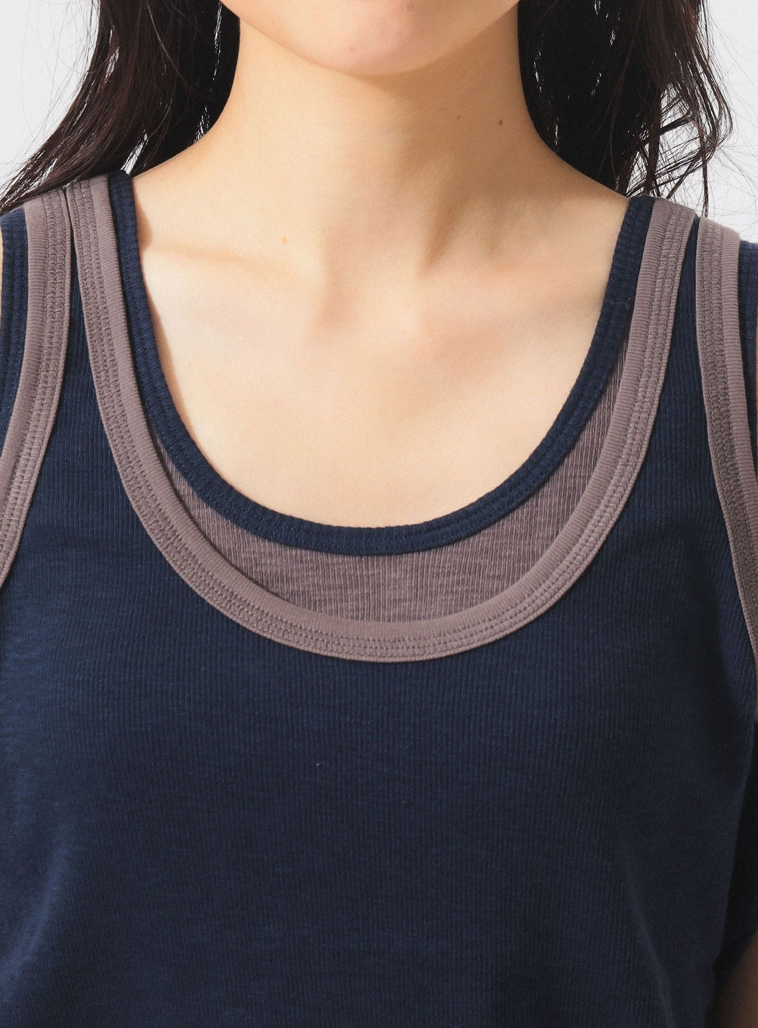A close-up of a person wearing the BEAMS BOY Layered Rib Tank Top in navy blue, featuring taupe trim around the neckline and armholes. The person's face is partially out of frame.
