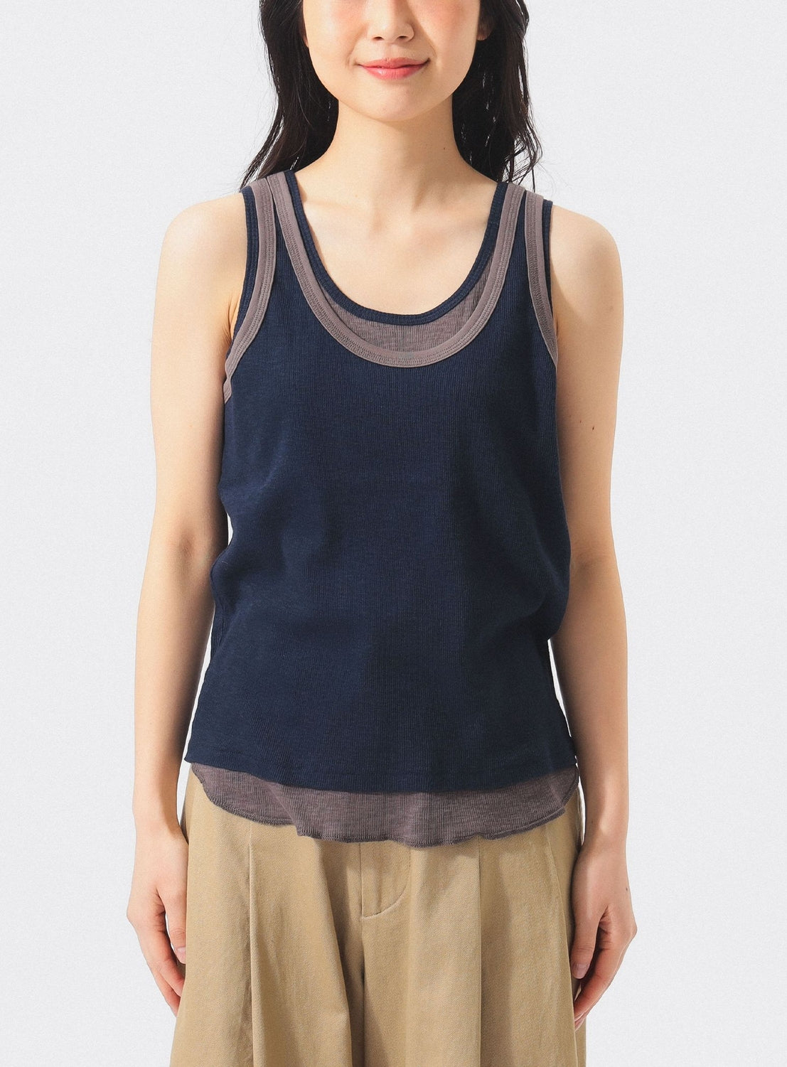 A person wearing the BEAMS BOY Layered Rib Tank Top, featuring navy blue ribbed knit fabric with beige trim, and light brown pants stands against a plain white background, facing forward.