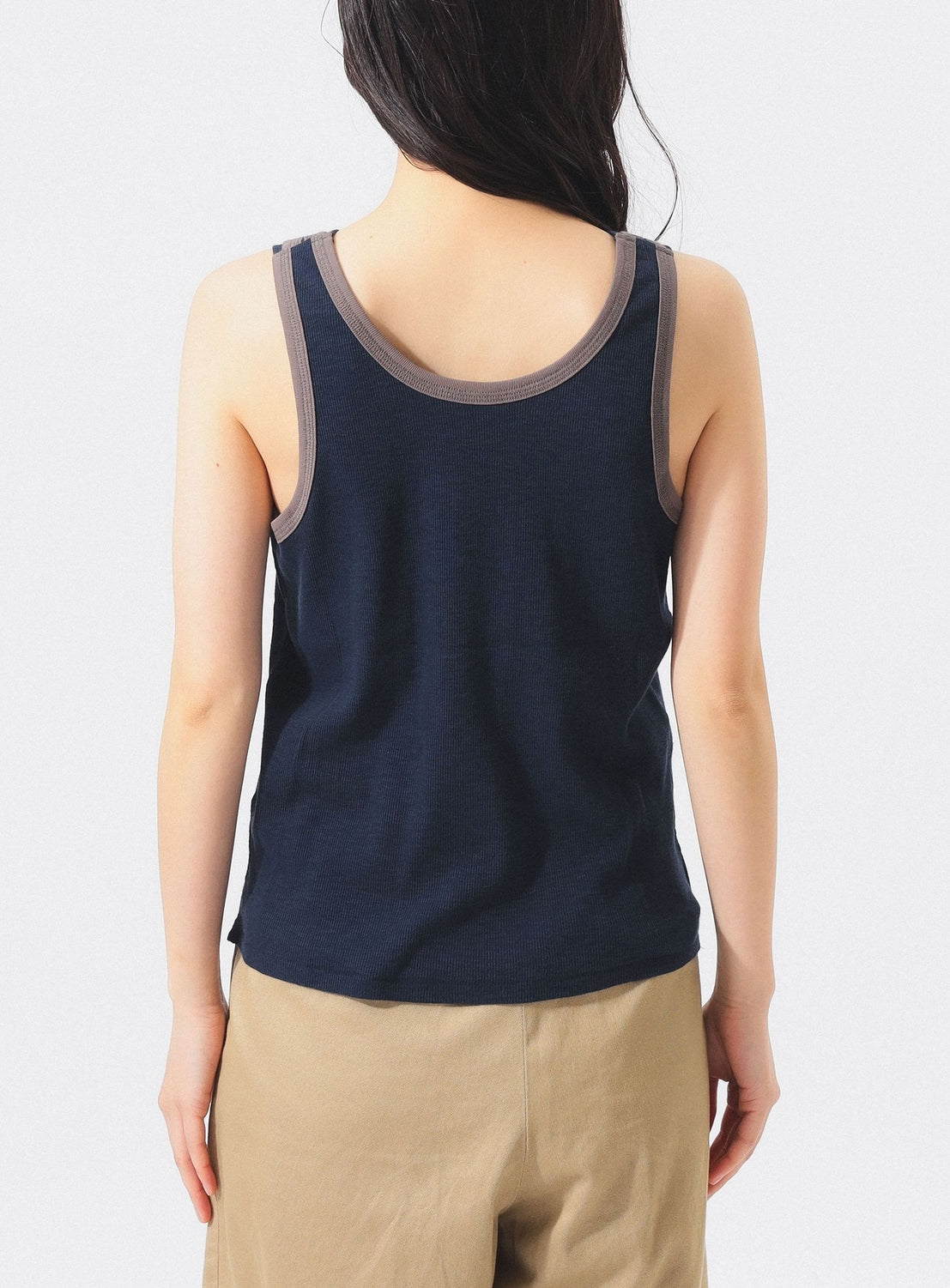 A person with long dark hair, seen from behind, wears the BEAMS BOY Layered Rib Tank Top in navy with gray trim and beige pants, standing against a plain light background.