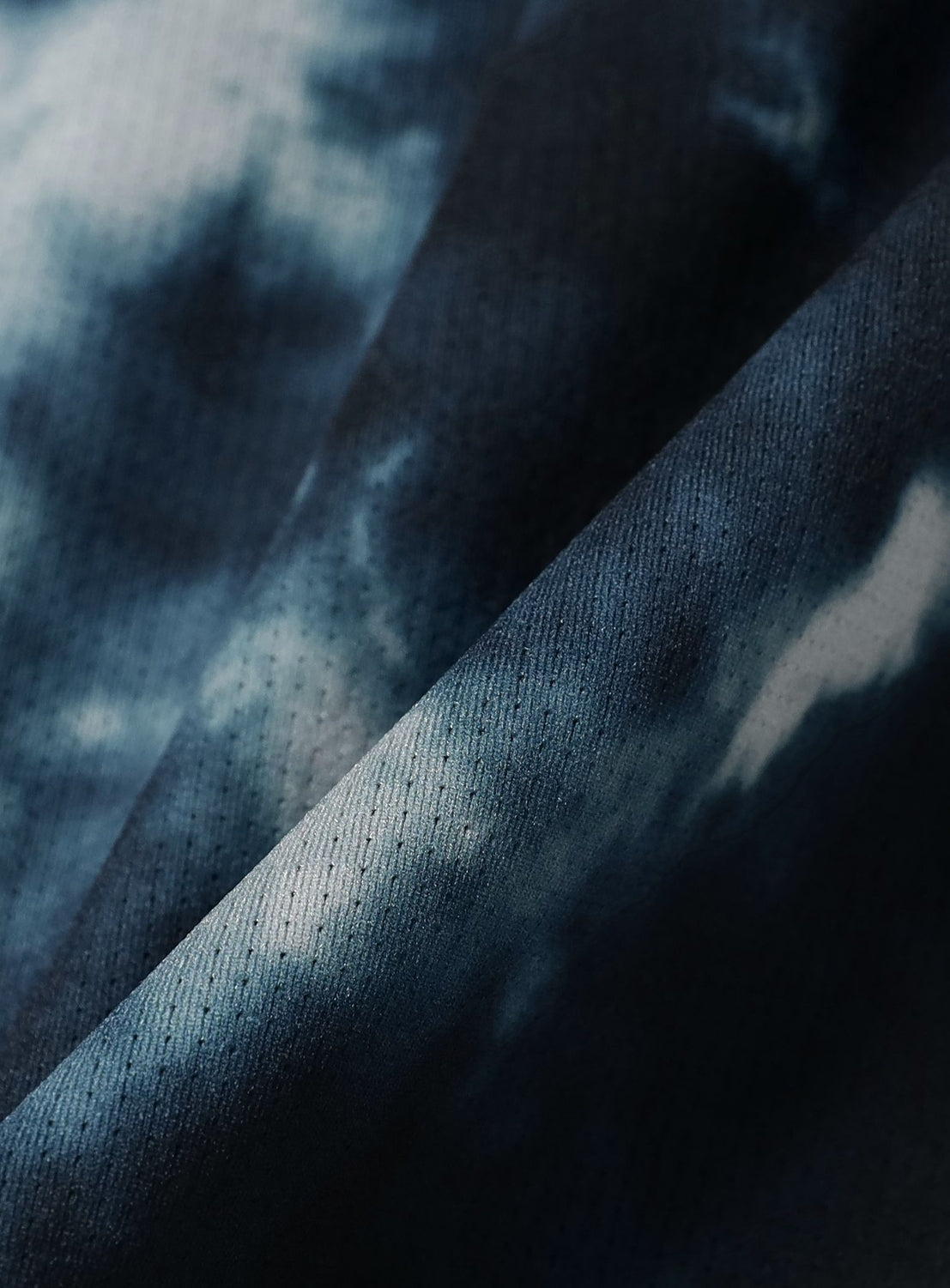 Close-up of dark blue and white tie-dye fabric with a soft, textured surface and subtle folds throughout, reminiscent of the UV-protective material featured in BEAMS' Wide Fit Dynamic Dry Shorts.