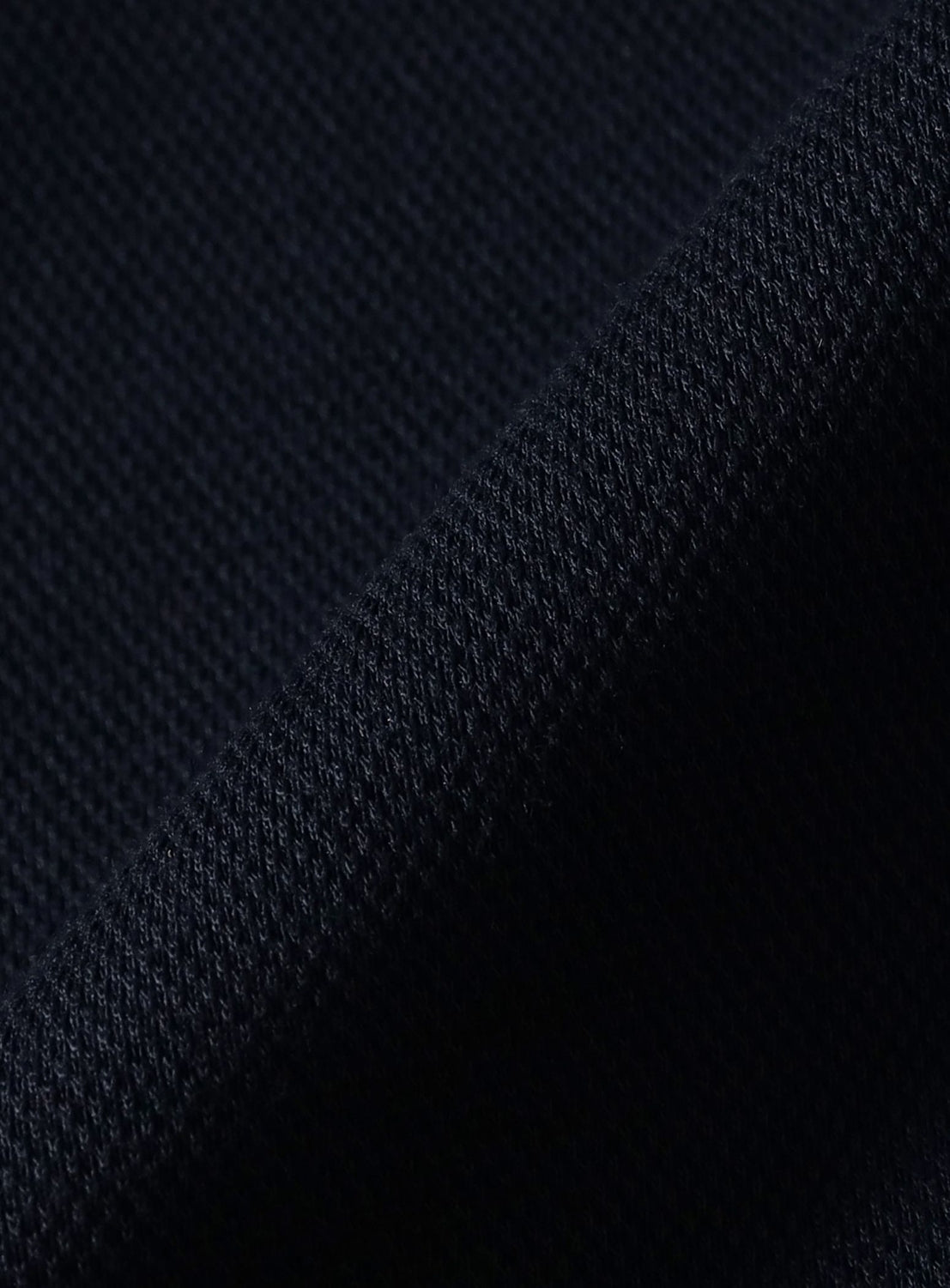 Close-up of navy blue pique knit fabric with a diagonal fold on an [Exclusive] BEAMS x Fred Perry Pique Long Sleeve Polo Shirt.