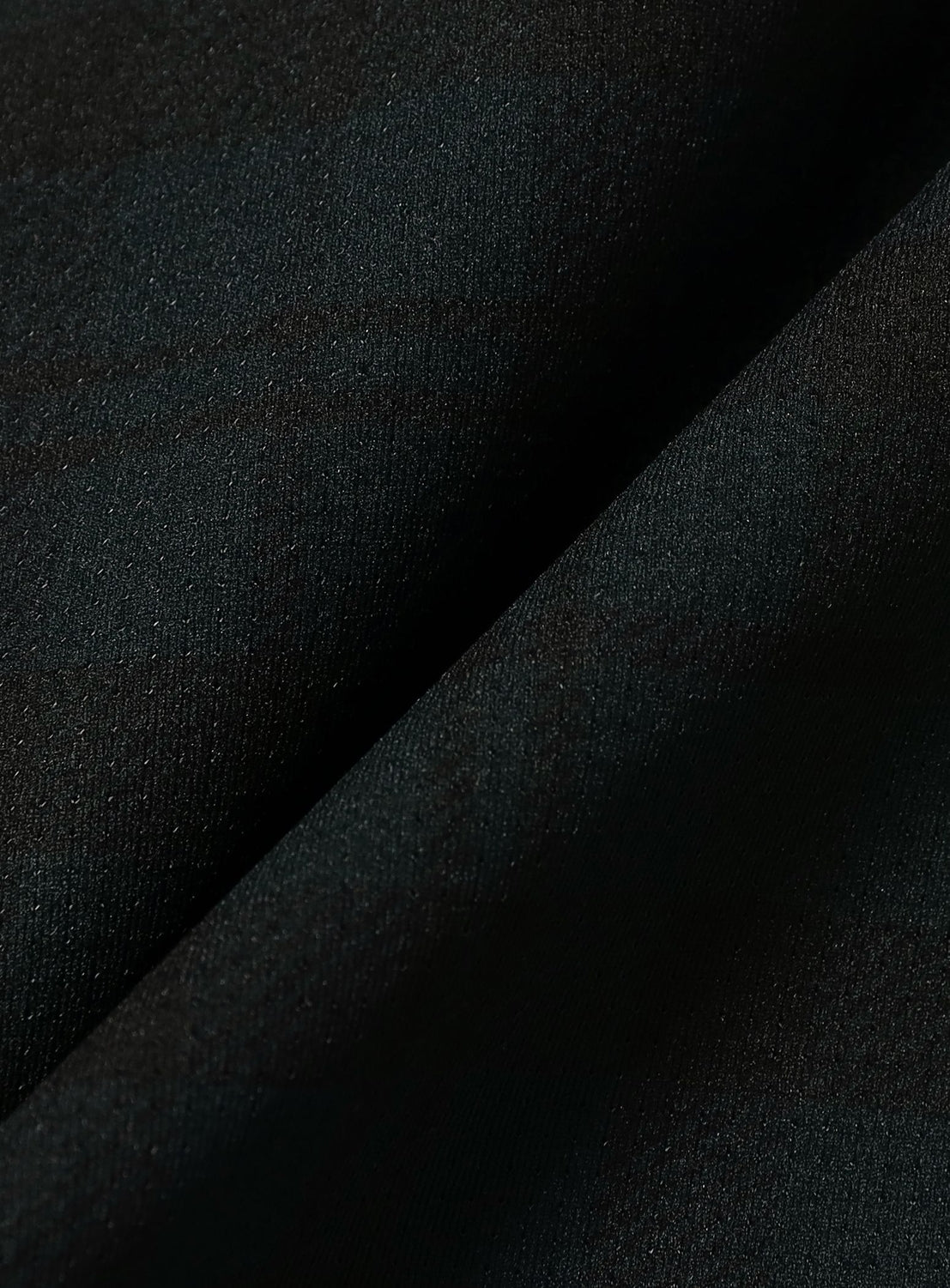 Close-up of dark, textured fabric with a diagonal crease running from the bottom left to the upper right, showing subtle variations in shading and weave detail—crafted from Dynamic Dry quick-drying fabric often used in BEAMS’ Wide Fit Dynamic Dry Shorts.