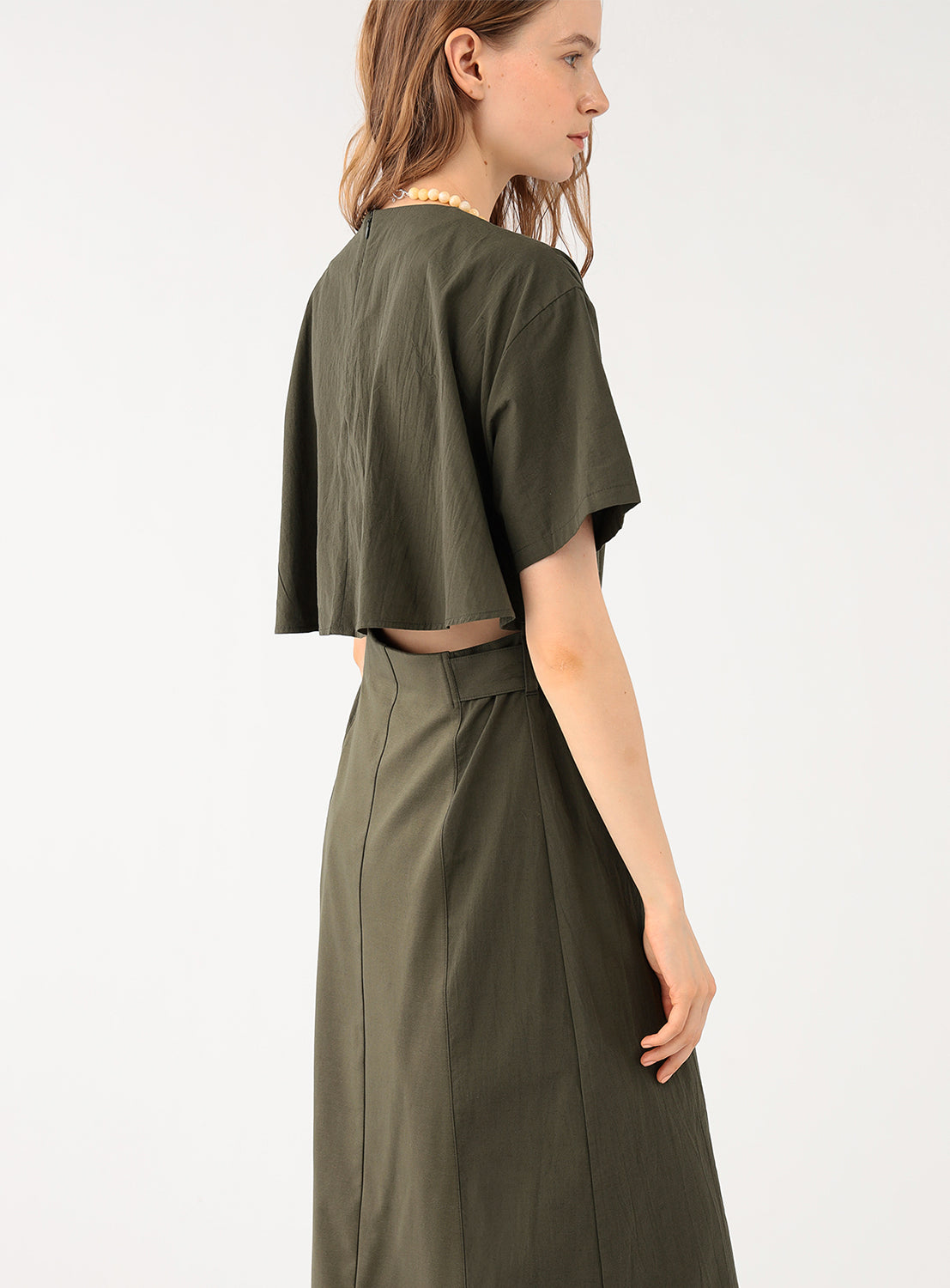 A female model wearing a khaki short-sleeved midi dress, shown from the side, revealing a tie waist.