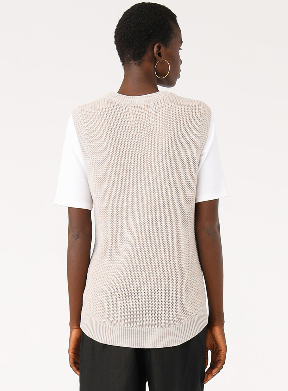 Back view of a model in the light grey knit vest, highlighting the layering over a white t-shirt.