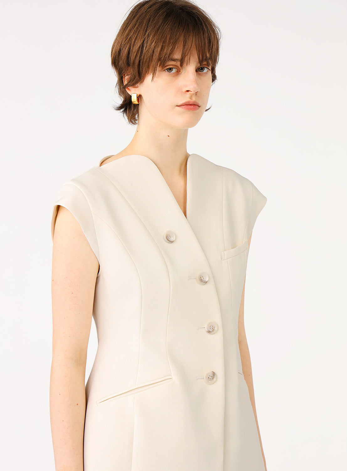 Female model wearing off-white tailored sleeveless vest, looking slightly to the side.