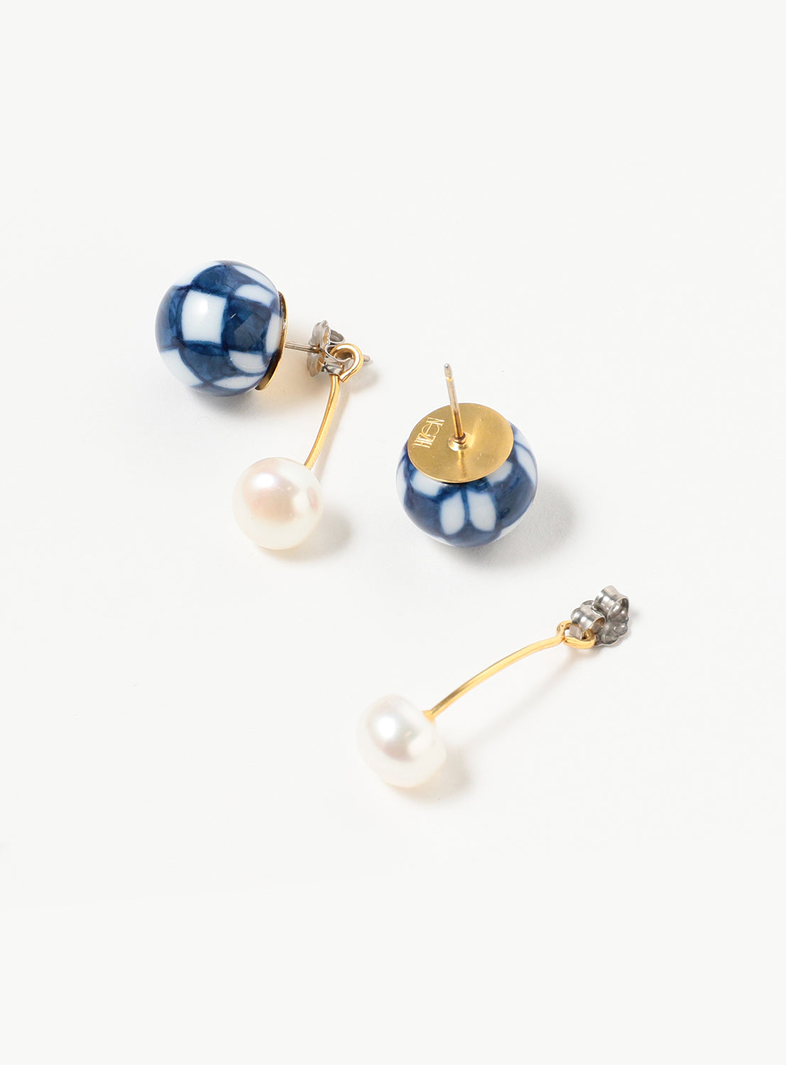 Arita Ware Motif & Baroque Pearl Earrings by Hizen Jewelry: one earring features a blue and white ceramic bead inspired by traditional Arita ware, reflecting exquisite Japanese craftsmanship, while the other showcases a luminous baroque freshwater pearl on a gracefully curved gold stem. Both earrings are finished with gold and silver backs and are displayed on a white background.