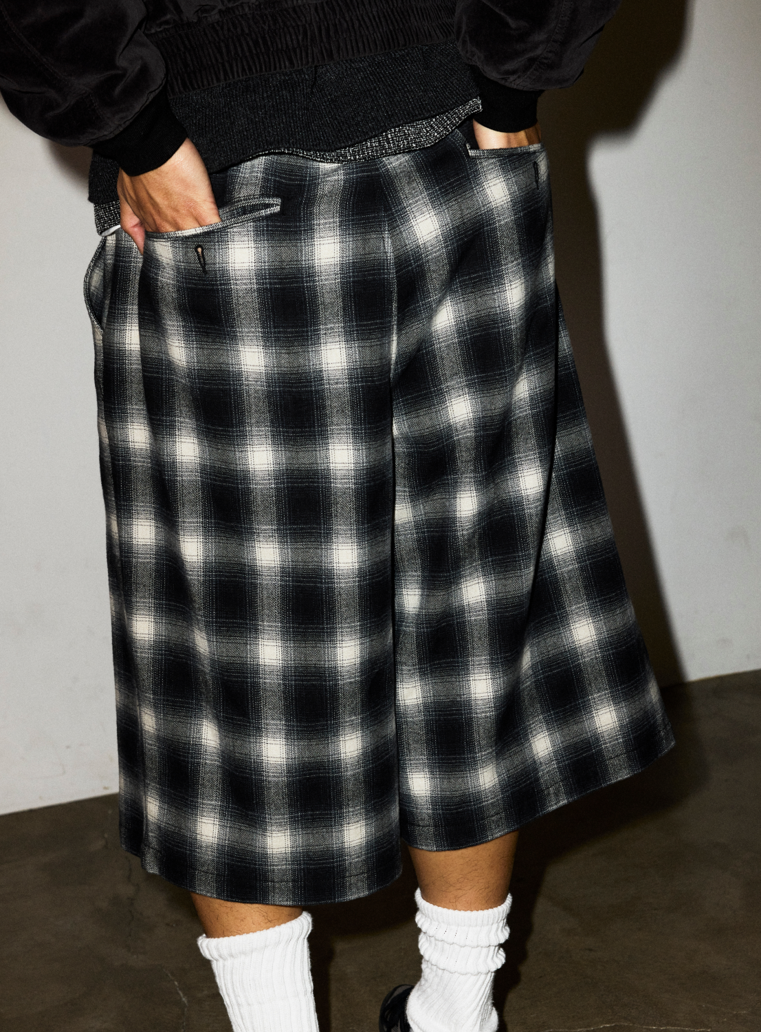 A person wearing relaxed fit, black and white ombre Check Shorts with their hands in the pockets.