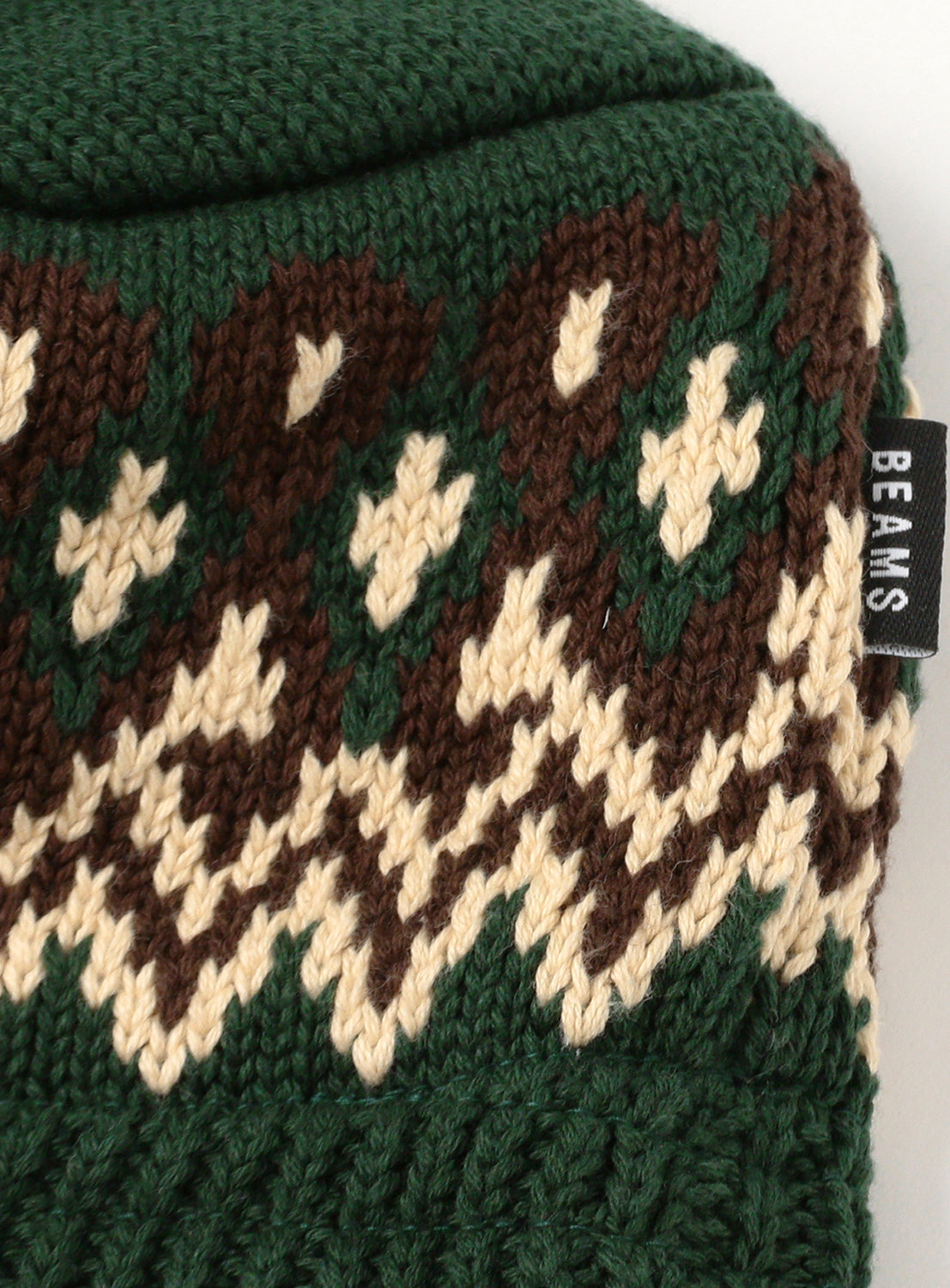 Close up of dark green knitted cap with beige and brown jacquard pattern.
