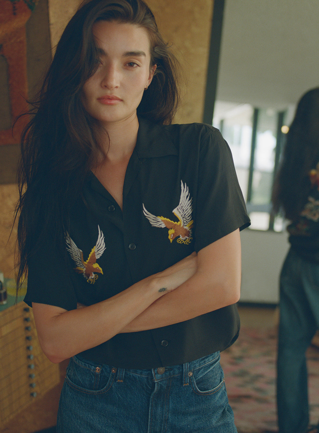 Model wearing a black shirt with eagle embroidery in an indoor setting.