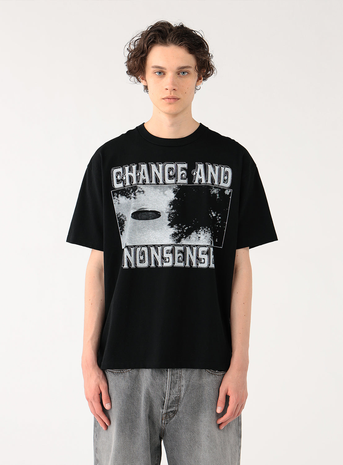 Model wearing a black t-shirt with "CHANCE AND NONSENSE" graphic and grey pants, front view, displaying casual fit.